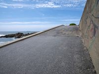 the sky over a long narrow road next to the ocean on the beach, which is painted with graffiti