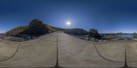 a tripod image of a road and some rocks and water underneath the sun on a clear day