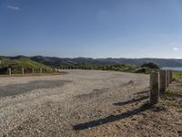 an empty road near some hills with mountains in the background with a blue sky with no clouds