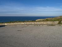 an empty paved road next to a sea front area with grass on the ground and a large cliff in the distance