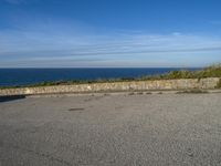 an empty paved road next to a sea front area with grass on the ground and a large cliff in the distance