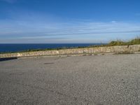 an empty paved road next to a sea front area with grass on the ground and a large cliff in the distance