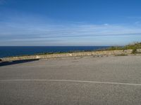 an empty paved road next to a sea front area with grass on the ground and a large cliff in the distance