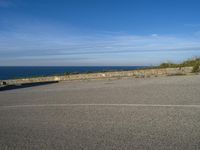 an empty paved road next to a sea front area with grass on the ground and a large cliff in the distance