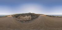 this is a fish eye view of some dirt road and mountains in the distance to the left and the sky to the right of the hill