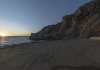 a lone person walking up a road next to the ocean and cliffs near sunset, on a clear day