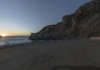 a lone person walking up a road next to the ocean and cliffs near sunset, on a clear day