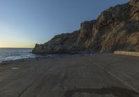 a lone person walking up a road next to the ocean and cliffs near sunset, on a clear day