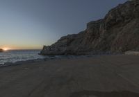 a lone person walking up a road next to the ocean and cliffs near sunset, on a clear day