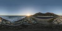 an image of a rock wall and road with the sun in the background on the beach