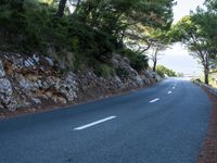 a paved highway curves around the edge of a cliff, with several trees behind it