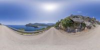 a fisheye lens view of the sea and coast on a mountain side road near rocks and trees