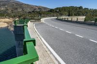 a winding highway surrounded by trees along the water's edge in spain with an airplane flying over it