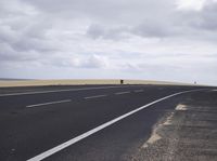 a empty highway in the middle of a desert area under cloudy skies and grey clouds