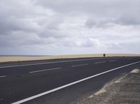 a empty highway in the middle of a desert area under cloudy skies and grey clouds