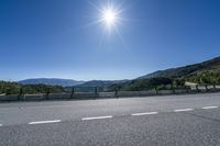 the bright sun shines brightly in the sky above a roadway and a mountain range