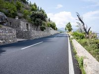 a long empty road between tall rocks and bushes by the ocean in greece on a sunny day