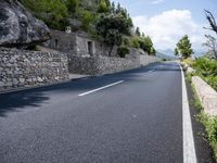 a long empty road between tall rocks and bushes by the ocean in greece on a sunny day