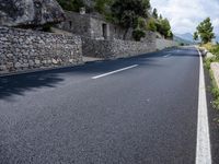a long empty road between tall rocks and bushes by the ocean in greece on a sunny day