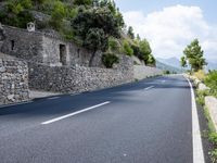a long empty road between tall rocks and bushes by the ocean in greece on a sunny day