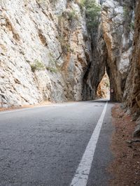 an open, empty mountain road lined by large rocky cliffs with tall trees on either side
