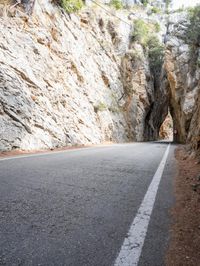 an open, empty mountain road lined by large rocky cliffs with tall trees on either side
