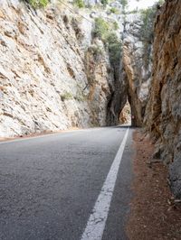 an open, empty mountain road lined by large rocky cliffs with tall trees on either side