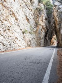 an open, empty mountain road lined by large rocky cliffs with tall trees on either side