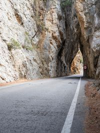 an open, empty mountain road lined by large rocky cliffs with tall trees on either side
