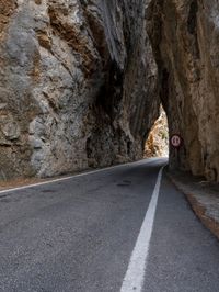 an open, empty mountain road lined by large rocky cliffs with tall trees on either side