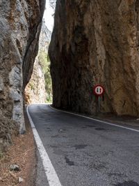 an open, empty mountain road lined by large rocky cliffs with tall trees on either side