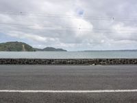 the street is full of cars along the shoreline with mountains in the distance on a stormy day