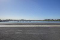 an empty airport runway with sun in the background by a body of water, and trees and a boat on the shoreline