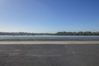 an empty airport runway with sun in the background by a body of water, and trees and a boat on the shoreline