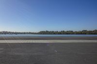 an empty airport runway with sun in the background by a body of water, and trees and a boat on the shoreline