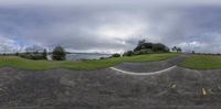 a panorama fish eye shot with the view down a road next to the beach and trees