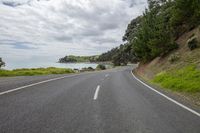 a paved road with trees and a body of water behind it, on a cloudy day