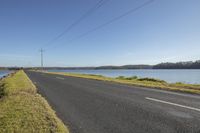 there is a road on the side of a body of water with telephone wires running across it