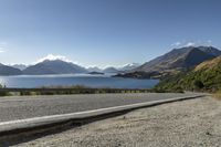 a paved road by a large body of water with mountains in the background and a road sign