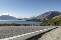 a paved road by a large body of water with mountains in the background and a road sign