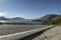 a paved road by a large body of water with mountains in the background and a road sign