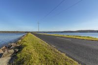 a road with power lines over the top of the water next to the road and a body of water