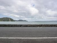 a body of water sitting between the rocks next to a road and telephone lines with an ocean on the far side