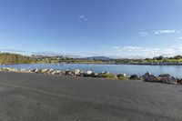 the empty road by the water is empty and there are rocks lining the street beside