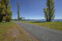 an empty road by the water and trees with green grass, with the mountains in the distance