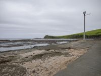 empty paved walkway and walking path at shoreline next to coastline with waves crashing on grassy hillside