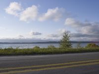 a long asphalt road that has water and a boat on it with grass in the foreground