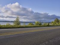 a long asphalt road that has water and a boat on it with grass in the foreground