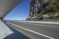 a view of an empty roadway from the side of a bridge near mountains and cliff tops