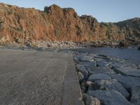 a skateboard parked on a large rocky beach near water at sunrise time with cliff in the background